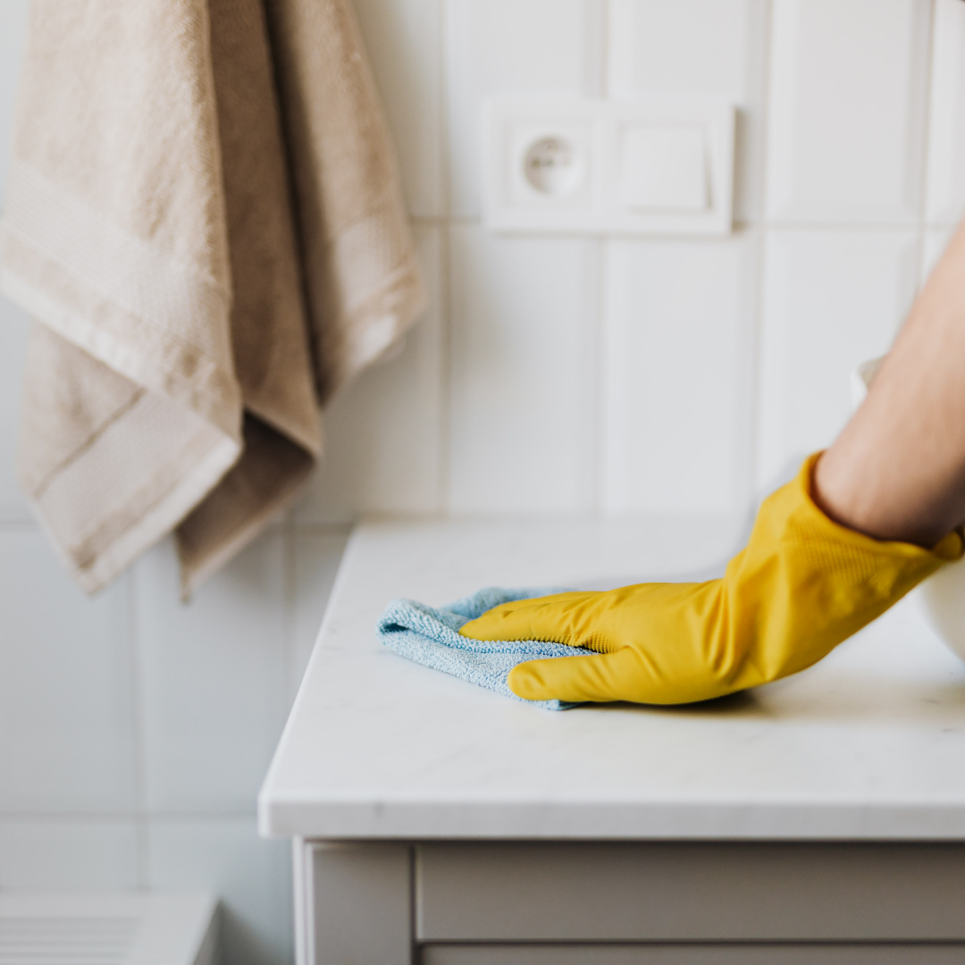 someone wearing yellow rubber gloves cleaning the bathroom vanity 